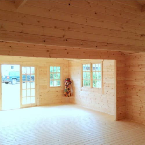 Interior view of roof, walls, window and double doors in 44mm log cabin, with floral mannequin in the corner.