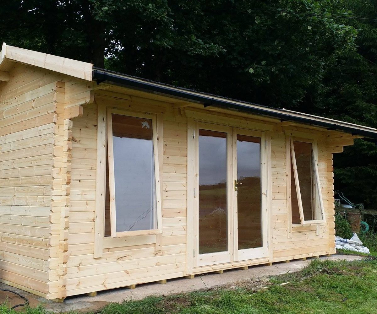 Log cabin with double doors, two open windows and apex roof, situated in a customer's garden.