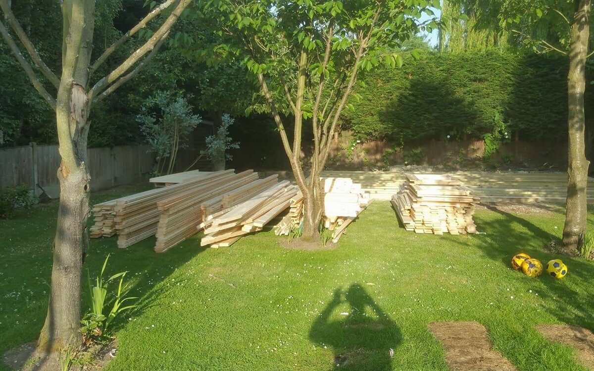 Log cabin kit laid out in a garden ready to be assembled.