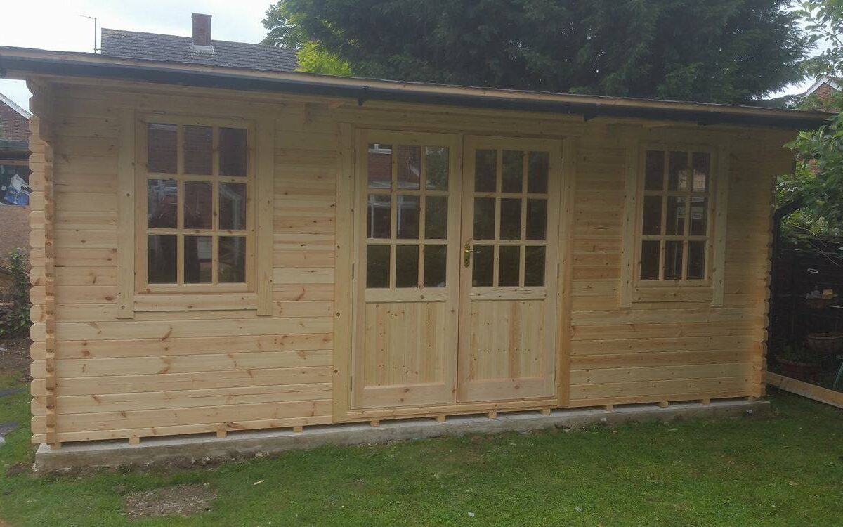Log cabin with double doors and two front windows, situated in customer's garden.