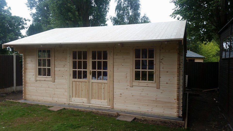 Log cabin with half glazed double doors, two front windows and overlapping apex roof.