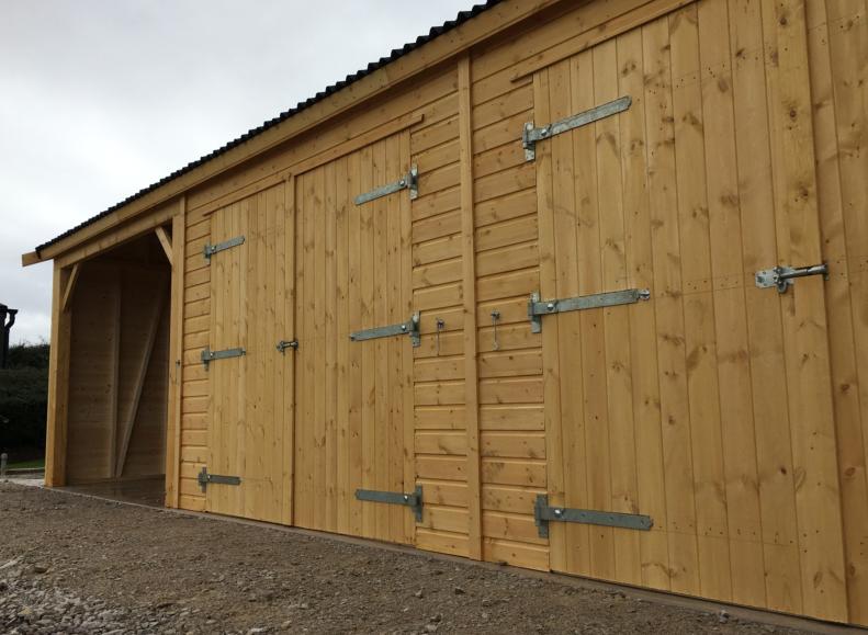 Wooden garage with lockable double doors and carriage house in a countryside setting.