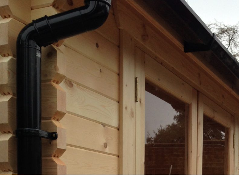 Close up of log cabin with full glazed double doors, black guttering and black pipe.