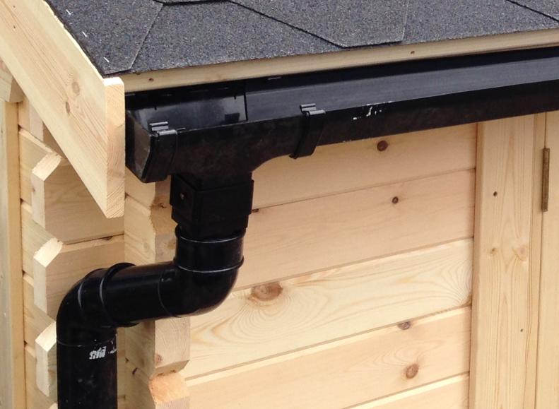 Close up of black guttering and black pipe on a log cabin with roofing shingles.
