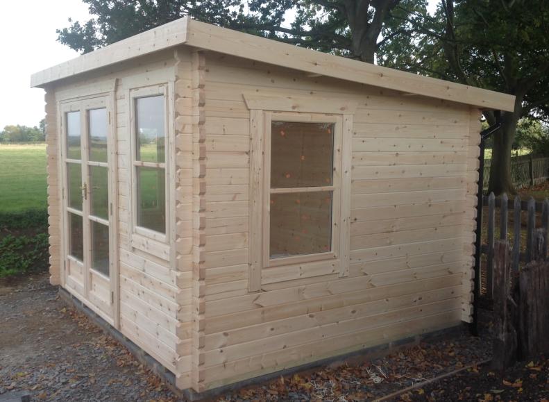 Newly constructed log cabin kit, with fully glazed double doors and window at the front, window at the side and pent roof.