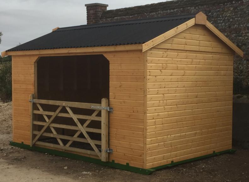 Wooden field shelter with wooden gate and felt apex roof, situated in farm yard.