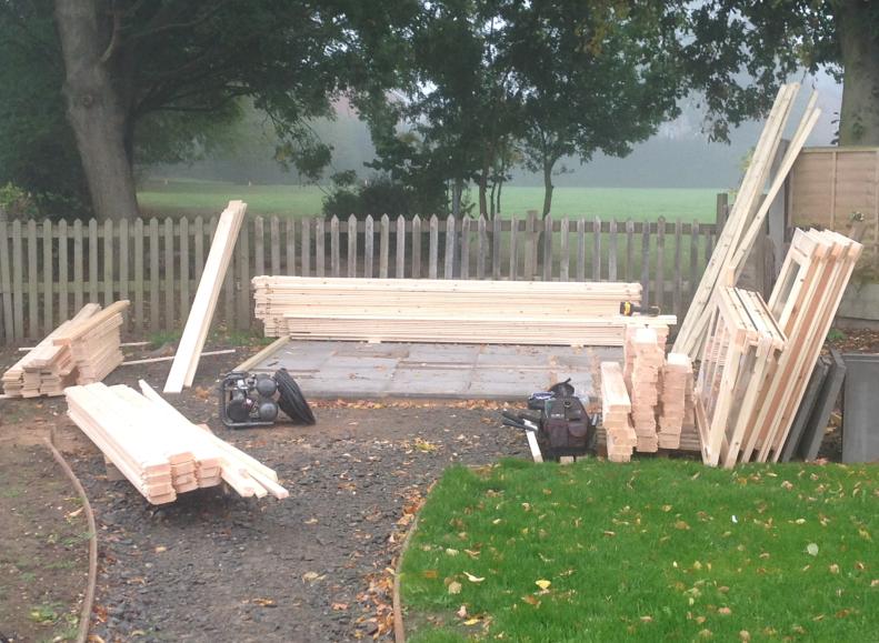 Log cabin kit laid out ready for assembly, organised into piles and with a solid base ready for construction.