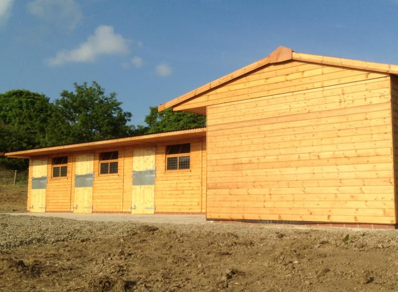 Wooden stables with apex roof in a countryside setting.