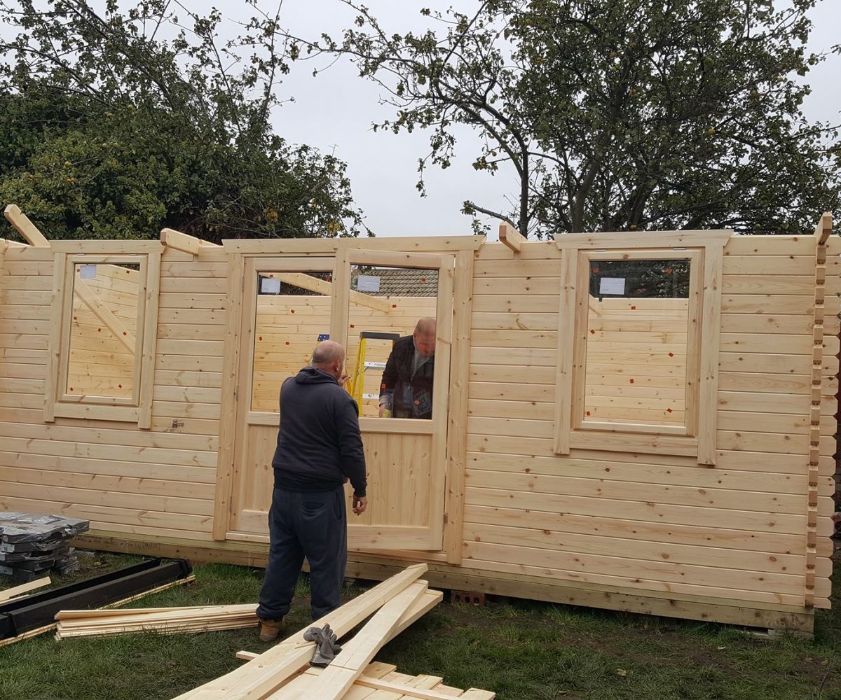 Two men building a log cabin in a customer's garden.